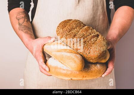 Un homme dans un tablier tient le pain frais dans ses mains avec de la croquant dorée. Maison boulangerie cuisson concept. Banque D'Images