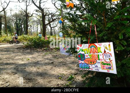 8 avril 2020, Southborough Common, Kent, Royaume-Uni: Messages pour les enfants remerciant le personnel du NHS et les principaux travailleurs accrochés à un arbre mis en place à l'intention de Southborough Common pendant le gouvernement a imposé la quarantaine / le verrouillage pour réduire la propagation du coronavirus. Les enfants de tout le pays ont mis des messages et des dessins d'arcs-en-ciel dans les fenêtres et ailleurs pour répandre l'espoir et encourager les gens à rester joyeux pendant la pandémie. Un garçon qui monte un vélo et sa famille peut être vu en arrière-plan. Banque D'Images