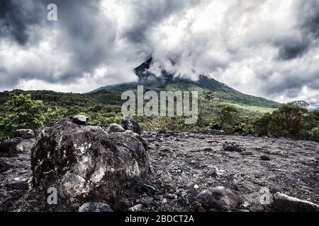 Pierres volcaniques avec volcan Arenal niché dans les nuages en arrière-plan. La Fortuna, Costa Rica.Volcano paysage. Banque D'Images