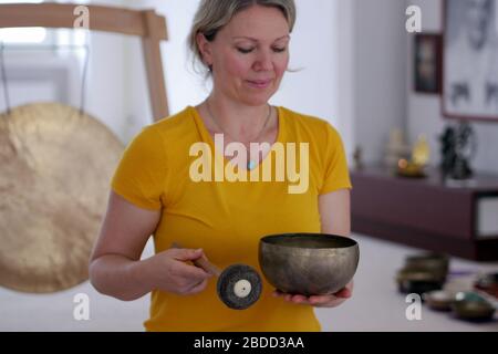 Gros plan sur une femme dans un tee-shirt jaune jouant au bol de chant tibétain. Banque D'Images