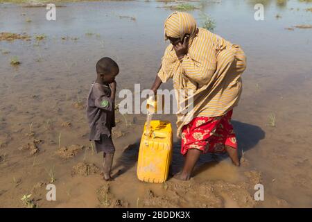 14.11.2019, Gode, région somalienne, Ethiopie - une femme ramasse l'eau d'une source d'eau naturelle dans un réservoir d'eau. Elle parle sur son téléphone portable Banque D'Images