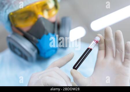 Le chercheur en matière d'usure de protection examine attentivement un échantillon sanguin dans un tube à essai. Recherche moderne en laboratoire. Création d'un vaccin. Gros plan. F Banque D'Images