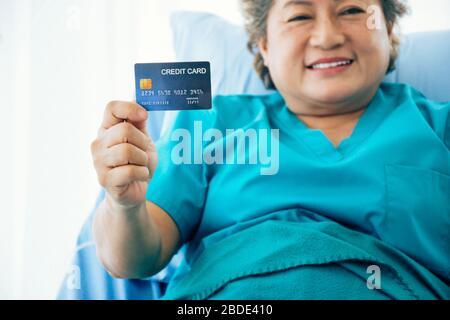 Une femme asiatique âgée montre une carte de santé/carte de crédit moqueuse alors qu'elle est allongé dans le lit à l'hôpital, foyer sélectif Banque D'Images