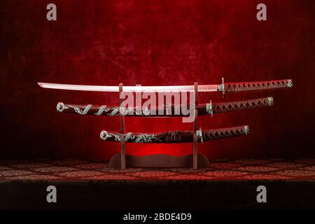 Trois épées sur le stand, lame de katana exposée, lumière rouge derrière Banque D'Images