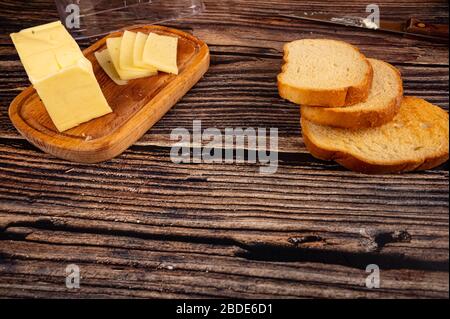 Pain grillé au blé frais et un plat à beurre en bois avec un morceau de beurre et des tranches de fromage sur fond en bois. Gros plan Banque D'Images