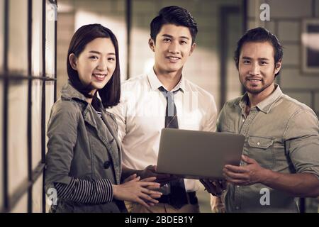 portrait d'un groupe de trois hommes d'affaires asiatiques réussis entrepreneurs se tenant au bureau regardant l'appareil photo souriant Banque D'Images