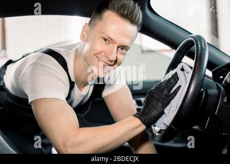 Nettoyage intérieur de voiture et détails en microfibre. Homme souriant et gai nettoyant l'intérieur de la voiture moderne, volant de voiture avec microfibre Banque D'Images