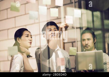 trois jeunes entrepreneurs asiatiques de petite entreprise se moquant de leurs discussions au bureau à l'aide de notes collantes Banque D'Images