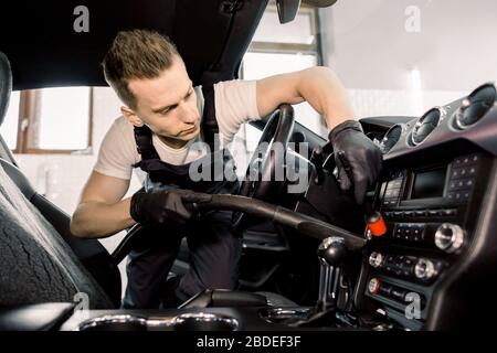 Jeune travailleur concentré, l'homme nettoie la poussière de l'intérieur de la voiture de luxe, à l'aide d'un aspirateur et d'une brosse spéciale. Concept de nettoyage et de détail de voiture, d Banque D'Images