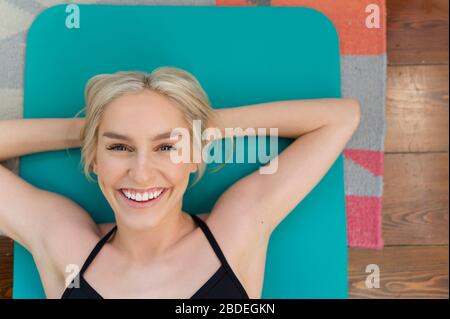 Femme blonde souriante couchée au dos sur un tapis de yoga Banque D'Images