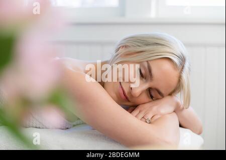 Femme souriante couchée avec les yeux fermés sur la table de massage Banque D'Images