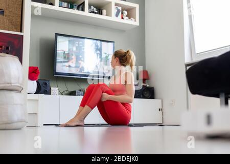 Jolie femme sportive travaillant à la maison, faisant des pilates exercice devant la télévision dans son salon. Distanciation sociale. Restez en bonne santé et Banque D'Images