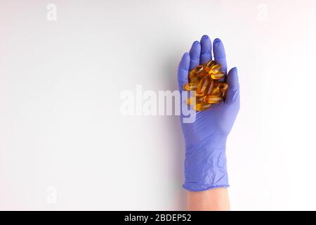 Les mains féminines dans le gant en caoutchouc de latex de couleur pourpre se trouvent dans les paumes de quelques capsules de vitamine de gel de softgel Omega 3 gel d'huile de poisson sur fond blanc Banque D'Images