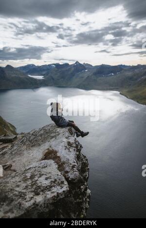 Norvège, Senja, Homme prenant des photos assis sur le bord de la falaise abrupte sur le sommet de la montagne Segla Banque D'Images