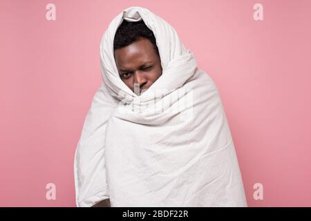 Beau homme afro-américain tenant une couverture qui veut dormir sur un mur rose. Banque D'Images