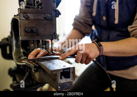 Selle femelle debout en atelier, sangle en cuir à coudre sur machine à coudre à la sellerie. Banque D'Images