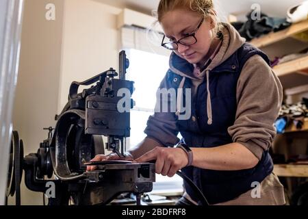 Selle femelle debout en atelier, sangle en cuir à coudre sur machine à coudre à la sellerie. Banque D'Images