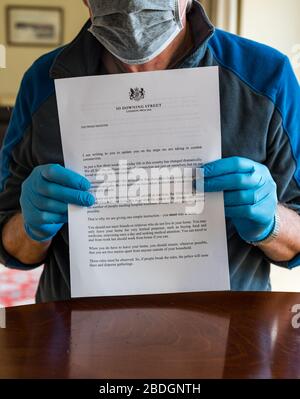 Homme portant des gants chirurgicaux et un masque de visage tenant la lettre du gouvernement HM de Boris Johnson au sujet de Covid-19 Coronavirus, Royaume-Uni Banque D'Images