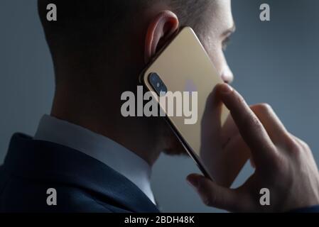 Zaporozhye. Ukraine. Février 2020. Gros plan portrait d'un jeune homme barbu dans un costume d'affaires tenant un iPhone XS dans sa main. Nouveau smartphone de Banque D'Images