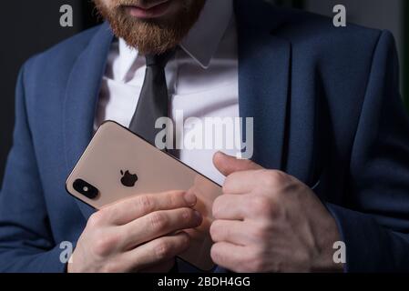 Zaporozhye. Ukraine. Février 2020. Gros plan portrait d'un jeune homme barbu dans un costume d'affaires tenant un iPhone XS dans sa main. Nouveau smartphone de Banque D'Images