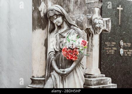 sculpture d'une femme avec des fleurs dans un vieux cimetière. Gros plan de l'ange lapié et du monument croisé au cimetière. Cimetière ancienne mère triste en pierre à l'ouest Banque D'Images