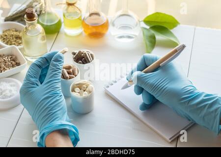 Capsules et ingrédients de compléments alimentaires. La main d'un pharmacien écrit dans un bloc-notes Banque D'Images