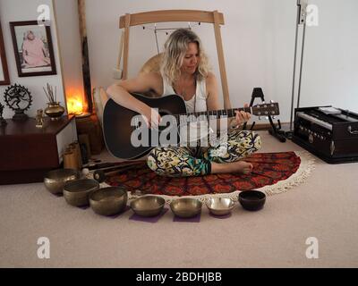 Jeune femme avec une guitare entourée d'instruments pour une séance de guérison sonore Banque D'Images