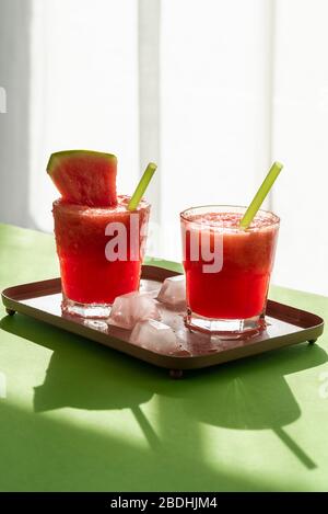 La limonade fraîche au melon glacé dans deux verres sur une table verte au soleil. Boisson fraîche d'été douce. Rafraîchissement du melon d'eau sur un plateau Banque D'Images