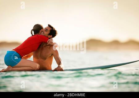 Femme à genoux sur un surf-board, embrassant son petit ami. Banque D'Images