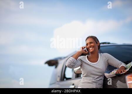 Femme parlant sur téléphone portable, penchant contre la voiture. Banque D'Images