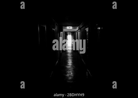 Image en noir et blanc avec un couloir d'humeur sombre avec des portes d'appartement de chaque côté - la lumière au bout du tunnel. Banque D'Images