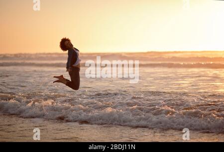 Portrait d'une femme en riant qui s'élatait dans l'air tout en se tenant au bord de la mer sur une plage. Banque D'Images