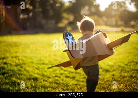 Le jeune garçon joue avec son avion de boîte en carton dans un jardin ensoleillé. Banque D'Images