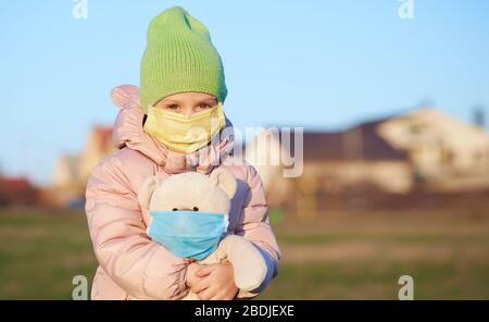 Petite fille d'enfant dans un masque de protection sur son visage tient un ours en peluche dans un masque. Quarantaine du coronovirus Banque D'Images