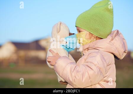 Petite fille d'enfant dans un masque de protection sur son visage tient un ours en peluche dans un masque. Quarantaine du coronovirus Banque D'Images