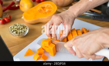 Les mains de l'homme trancher la citrouille sur des cubes sur le tableau de découpe Banque D'Images