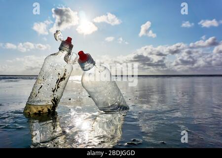 Bouteilles en plastique avec bouchons rouges pour bouteilles debout dans la mer avec ciel bleu et contre-jour à marée basse. Concept de pollution plastique de la mer. Banque D'Images