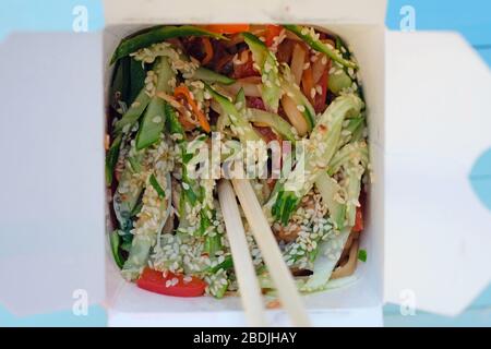 Nouilles chinoises aux légumes et à la viande saupoudrées de graines de sésame dans une boîte en carton vue de dessus. Wok plats dans des boîtes en carton pour la maison de nourriture. Banque D'Images