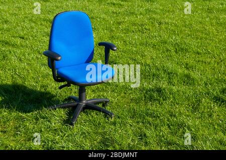 Chaise de bureau en tissu bleu vide, debout à l'extérieur au milieu d'un champ vide d'herbe verte Banque D'Images