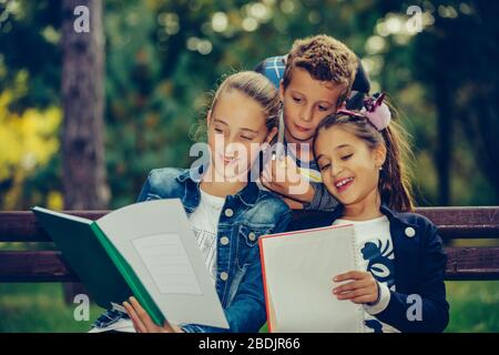 Retour à l'école. Les enfants avec des sacs à dos ont du plaisir, de parler, de lire un livre.Groupe d'écoliers élémentaires ayant une discussion sur les devoirs pendant qu'ils sont assis Banque D'Images