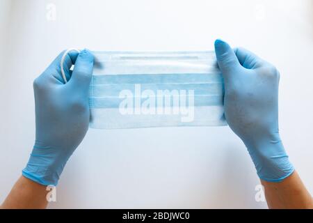 Vue de la première personne d'une femme tenant un masque facial sur un fond de table blanc. Masque de protection pour la propagation du virus. Gros plan, espace de copie, vue de dessus, plat. Banque D'Images