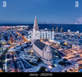 Vue sur l'immense bâtiment de l'église avec grande tour blanche dans le quartier lumineux de Reykjavik avec l'océan en arrière-plan au crépuscule Banque D'Images