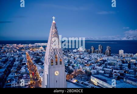 Vue aérienne de la tour moderne blanche de la grande église Hallgrimskirkja avec croix luglisante dans le centre-ville moderne au crépuscule en Islande Banque D'Images