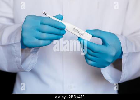 Gants de médecin masculin montrant le thermomètre. Médecin avec thermomètre dans les mains. Gros plan du thermomètre. Vie saine, docteur, concept de virus. Banque D'Images