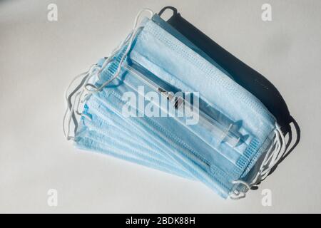 Seringue avec vaccin bleu et ampoule sur le masque médical. Fond blanc Banque D'Images