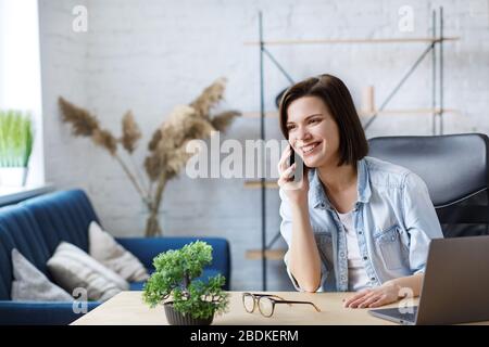 Travailler en ligne à partir de home.Communication avec des collègues et des indépendants.Portrait de jeunes indépendants de sexe féminin parlant sur smartphone et souriant. Concept Banque D'Images