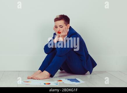 Déprimé fatigué malheureuse femme d'affaires assis sur le sol avec des papiers de projet contrat donnant l'air sombre isolé dans sa maison de chambre lumineuse. Travail à Banque D'Images