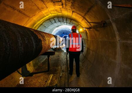 Le travailleur du tunnel examine le pipeline dans le tunnel souterrain Banque D'Images