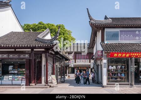 Suzhou Chine - 3 mai 2010: Rue commerçante avec des bâtiments traditionnels bas blanc et gris comme petits commerces. Piétons marchant. Feuillage vert et bleu Banque D'Images
