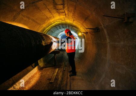 Le travailleur du tunnel examine le pipeline dans le tunnel souterrain Banque D'Images